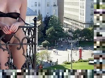 A woman undresses on a balcony in the city center. Public flashing.