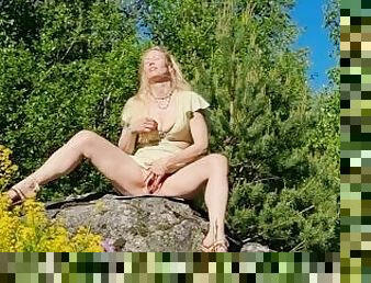 Horny MILF masturbating in a summer dress on top of a huge rock in a public park at midsummer