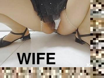 A married woman wearing a one-piece dress and pantyhose squats down, pulls aside her panties, and ex